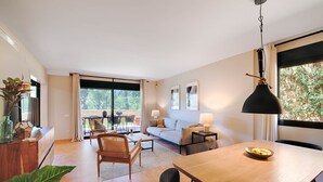 Una sala de estar moderna con sofá, mesa de comedor y sillas, un ventanal con vistas a zonas verdes, y un puerta corrediza de vidrio que da a un espacio al aire libre.