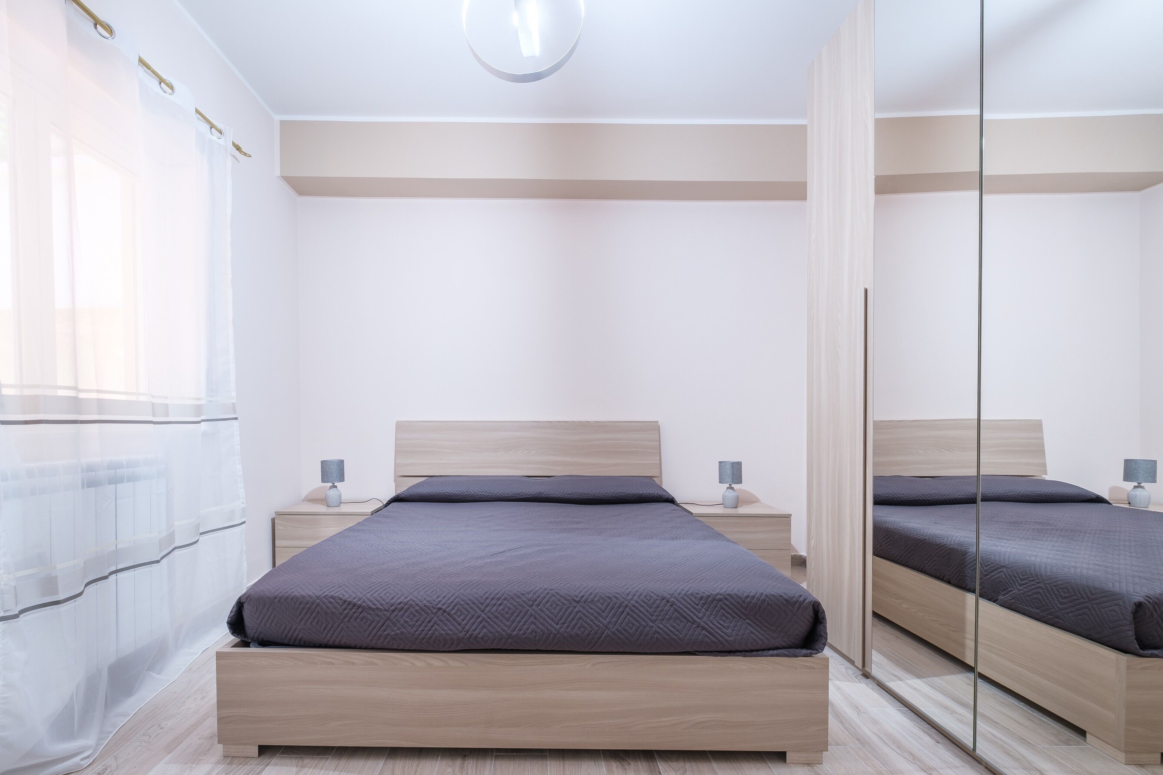 Une chambre moderne avec un grand lit, des tables de chevet, un miroir et un luminaire au plafond.