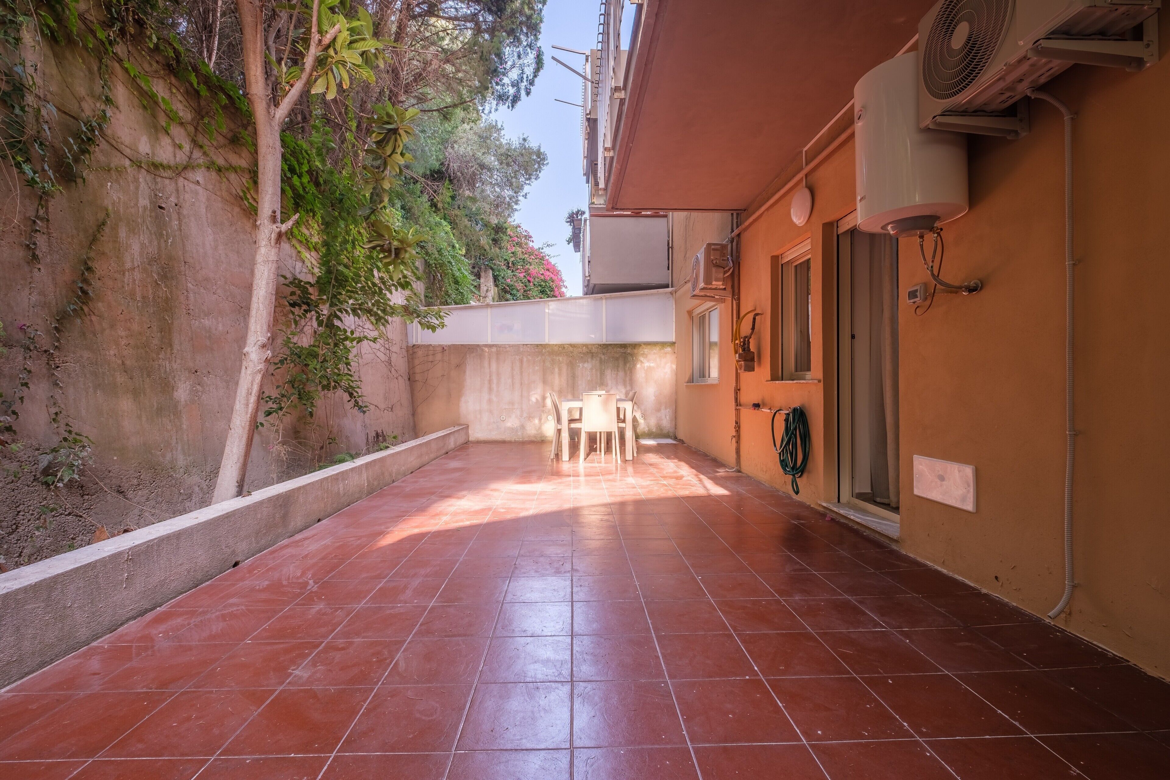 Une cour avec un sol carrelé, une table et des chaises, et un mur sur lequel est installé un appareil de climatisation.
