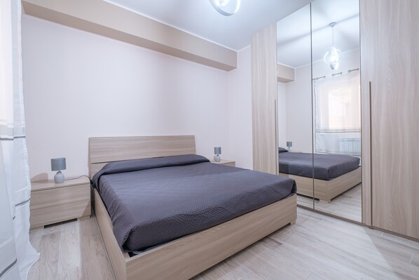 A modern bedroom with a bed, nightstands, a mirror, and a wardrobe.