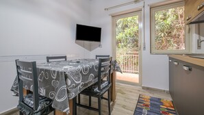 Un área de comedor con una mesa, sillas, un televisor montado en la pared y vistas a un jardín a través de una puerta corrediza.