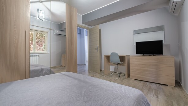 Un dormitorio moderno con cama, escritorio, silla, televisor y aire acondicionado.