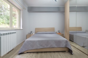 Une chambre à coucher avec un lit, des tables de chevet, un miroir, un radiateur et une fenêtre.