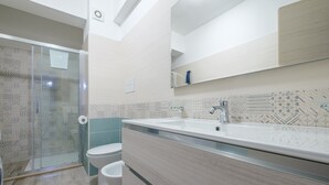 Un baño moderno con ducha, inodoro, tocador y un espejo grande.