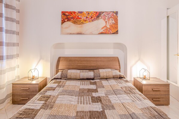A bedroom with a wooden headboard, a quilted bedspread, two bedside tables with lamps, and a painting above the bed.