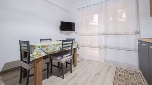 Un comedor con una mesa dispuesta para cuatro, un televisor montado en la pared y una ventana con cortinas translúcidas.