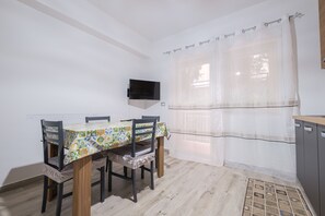 A dining area with a table set for four, a television mounted on the wall, and a window with sheer curtains. - Holiday Apartment "Damilhouse 3" with Balcony and Wi-Fi (Messina)