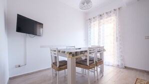 Un coin repas avec une table et des chaises, un téléviseur à écran plat fixé au mur et une fenêtre agrémentée de rideaux à motifs.