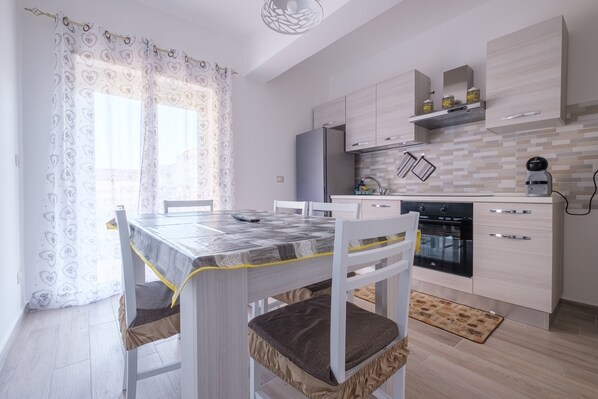 A modern kitchen with a dining table, chairs, and a refrigerator.