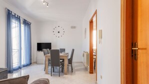 Ein modernes Wohnzimmer mit einer Couch, einem Esstisch mit Stühlen, einem Fernseher und einer Wanduhr.