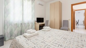 Ein Hotelzimmer mit Bett, Schreibtisch mit Computer, Fernseher, Kleiderschrank und einem durchgegangenen Tür erkennbaren Badezimmer.
