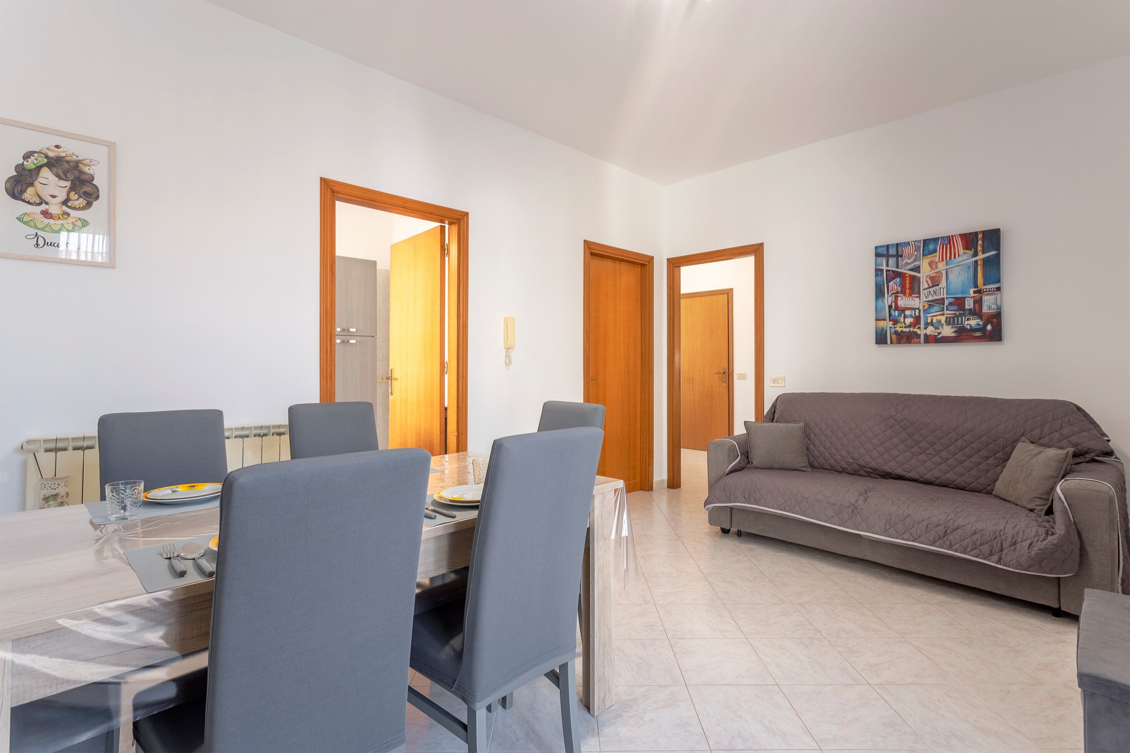 Un coin repas avec une table dressée pour quatre personnes, un canapé et deux portes donnant sur d’autres pièces.