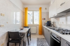 A compact kitchen with a dining table, chairs, a stove, and a window with curtains. - Holiday Apartment "Contessa Vacanze Byron" with Mountain View, 2 Balconies and Wi-Fi (Contessa Entellina)