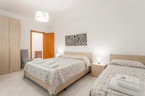 A bedroom with two beds, a wardrobe, a chair, a bedside table with a lamp, and a wall art piece. - Holiday Apartment "Contessa Vacanze Byron" with Mountain View, 2 Balconies and Wi-Fi (Contessa Entellina)