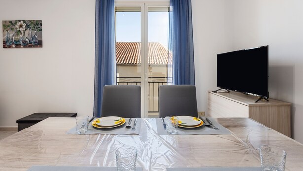 Ein Essbereich mit Tisch für zwei Personen, einem Fernseher und Blick auf einen Balkon.