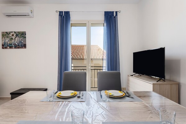 A dining area with a table set for two, a television, and a balcony view.