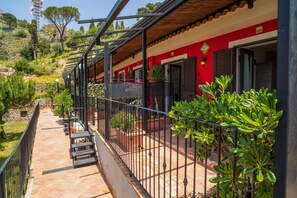 A red building with a balcony, potted plants, and a stone pathway.