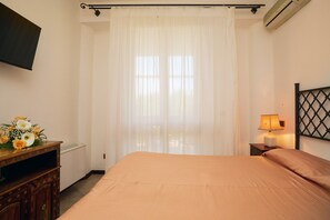 A hotel room with a bed, a bedside table with a lamp, a wall-mounted TV, and a decorative vase with flowers.
