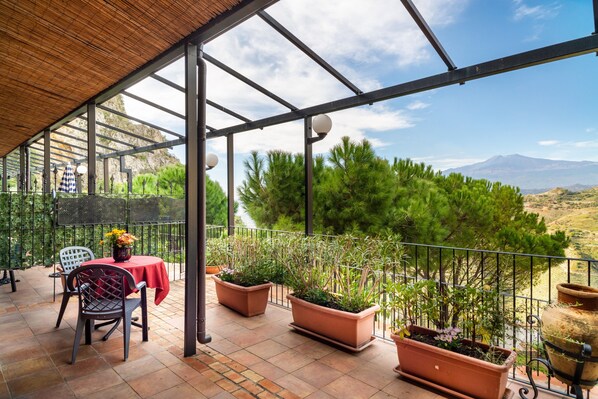 Un espace extérieur abrité, doté d’une table et de chaises, de plantes en pot et offrant une vue sur un paysage montagneux.