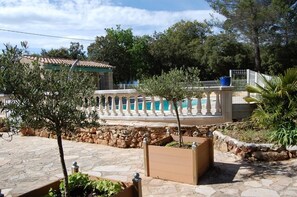Une zone pavée de pierres, avec une piscine, un petit arbre et un bâtiment doté d’un toit en tuiles.