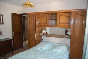 Un dormitorio con cama, armario de madera y lámpara en una mesita de noche.
