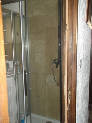 Une douche avec une porte en verre, des murs recouverts de carreaux beiges et un cadre de porte en bois.