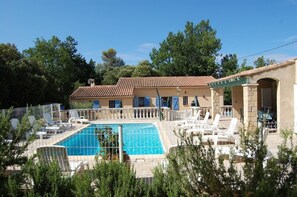 Zona de piscina con sillones reclinables, una piscina y un edificio con techo de tejas.