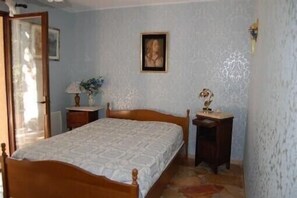 Une chambre à coucher avec un lit en bois, une table de chevet, une commode, un tableau encadré au mur et une porte.