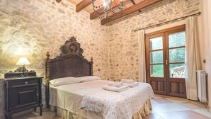 Camera con pareti in pietra, un letto, un comodino, una lampada e vista all'esterno tramite una porta.