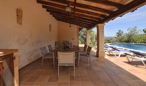 A covered patio with a table and chairs, a pool, and a view of the landscape.