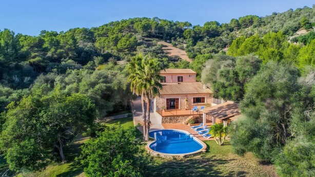 Una casa circondata da alberi e colline, con una piscina.