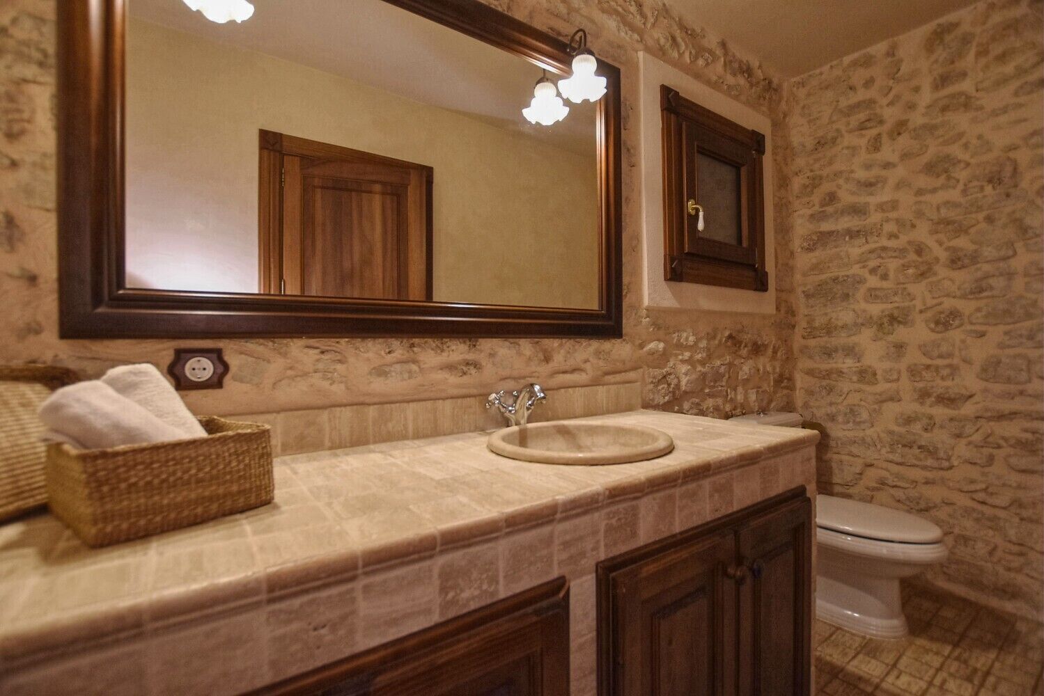 Une salle de bain avec un mur en pierre, un meuble-lavabo en bois, un miroir et des toilettes.