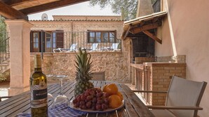 Un patio con tavolo apparecchiato per un pasto, una bottiglia di vino e un piatto di frutta.