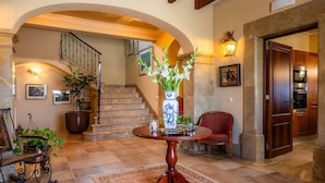 A spacious lobby with a grand staircase, a round wooden table with a vase, and a red chair. - Holiday Home 'Can Corem De Son Moix' with Mountain Views, Wi-Fi and Air Conditioning (Manacor)