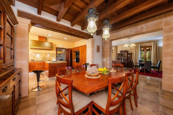 A spacious dining area with a wooden table and chairs, a kitchen in the background, and a chandelier.