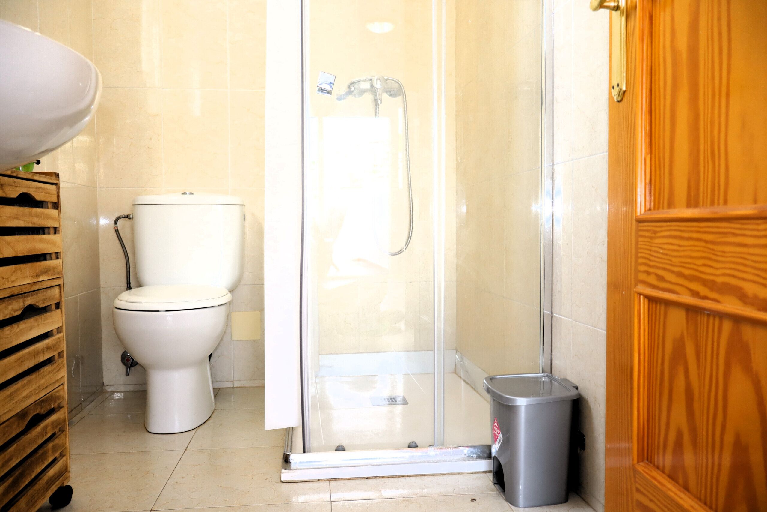 Un baño con inodoro, cabina de ducha y cubo de basura.