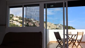 Ett rum med en skjutdörr i glas som leder ut till en balkong med ett bord och stolar, med utsikt över en sluttning med byggnader.