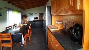 Una cocina con armarios de madera, una mesa de comedor con sillas, un refrigerador y una cafetera.