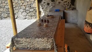 Una pared de piedra, una mesa de madera con superficie de guijarros y una zona de cocina con un lavabo y un recipiente azul.