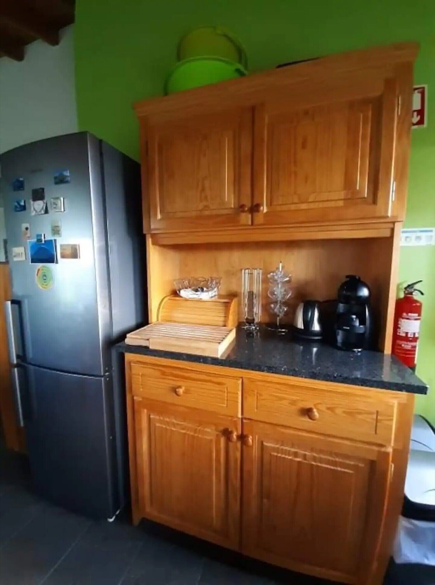 A kitchen with wooden cabinets, a refrigerator, a coffee maker, and a fire extinguisher.