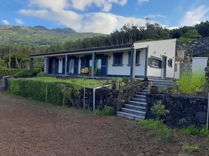 A modern two-story house with a stone staircase leading to the entrance, surrounded by greenery and hills in the background.