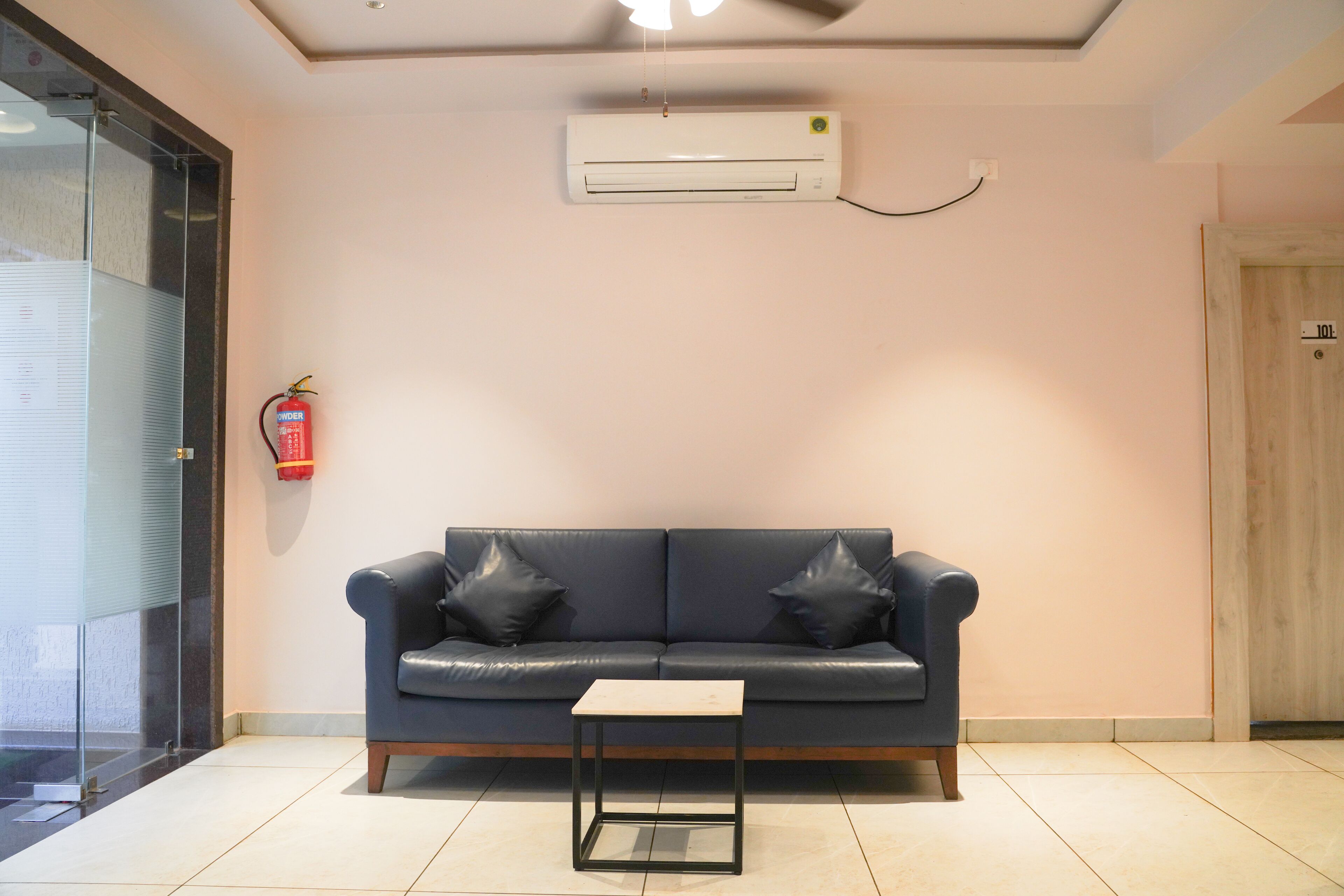 A modern living room with a dark blue leather sofa, a small black table, and a white air conditioning unit mounted on the wall.