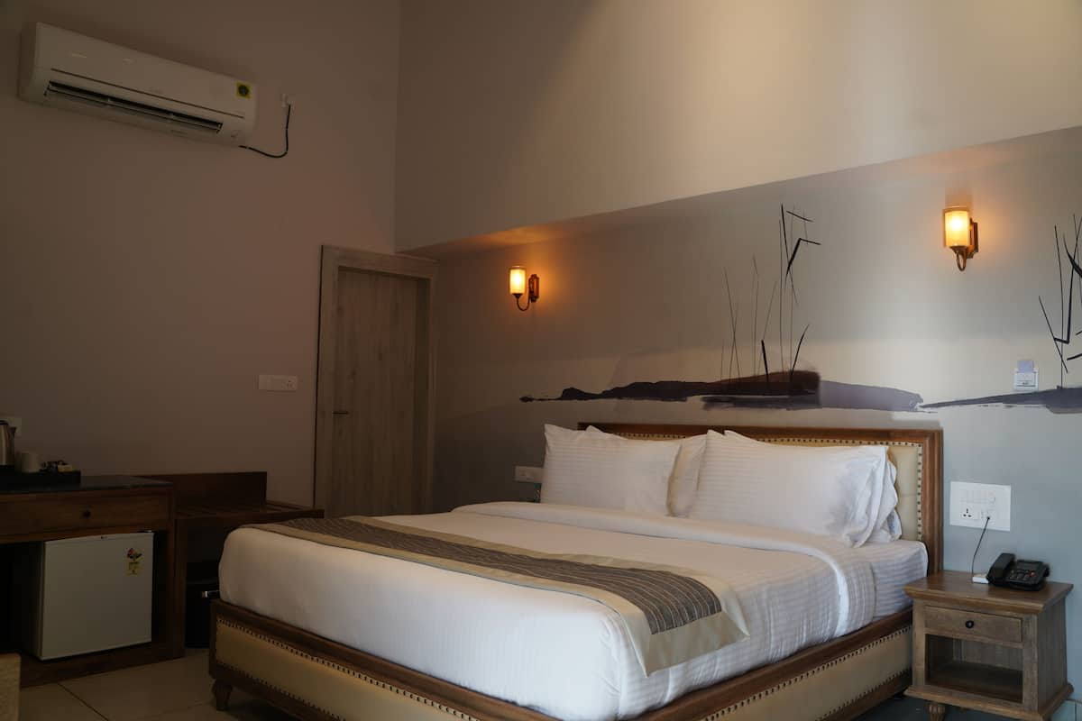 A hotel room with a bed, bedside table, nightstand, wall-mounted air conditioner, and two wall sconces.