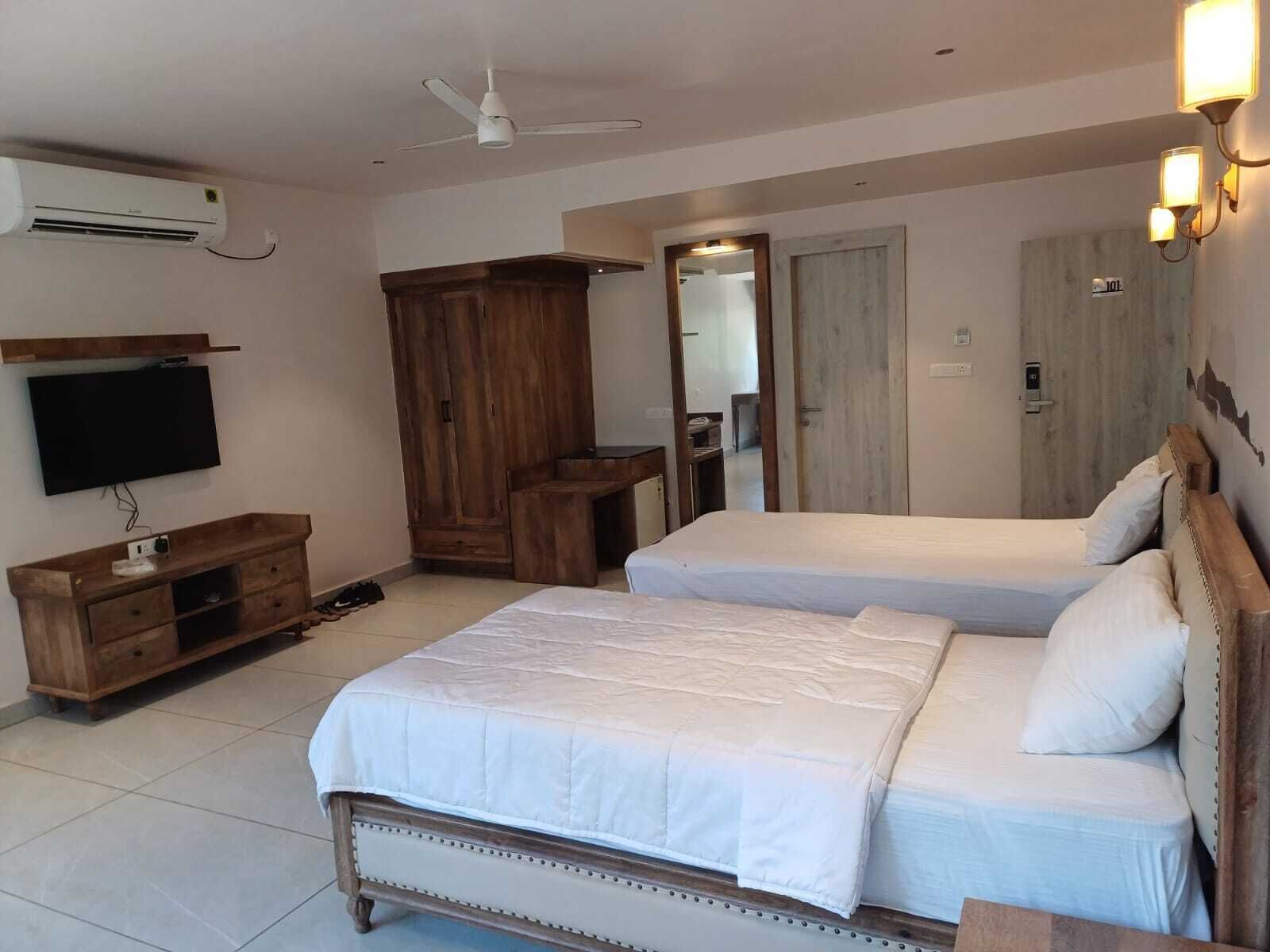 A bedroom with two beds, a wardrobe, a television, and a ceiling fan.