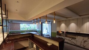 A modern bar area with a marble countertop, hanging light fixtures, and a view of the outdoors through large windows. - Ariena by ABA Hotels (Morjim)