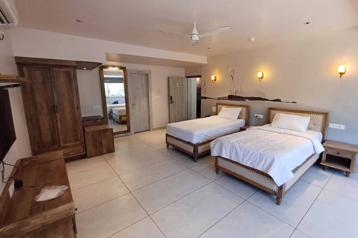 A hotel room with two beds, a wooden wardrobe, a desk, and a ceiling fan.