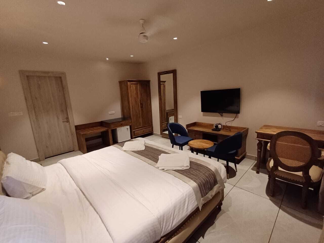A hotel room with a large bed, a desk, a chair, a television, and a wardrobe.