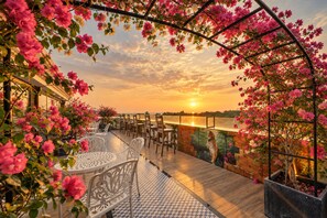 An outdoor seating area with tables and chairs, overlooking a body of water, under a metal pergola with flowering plants. - HARRY PHU QUOC HOTEL 3 (Phu Quoc)