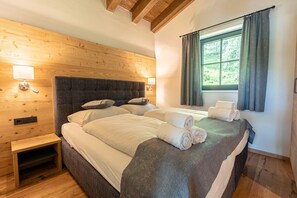 Una cama doble con cabecera de madera, una mesita de noche y una ventana con cortinas.