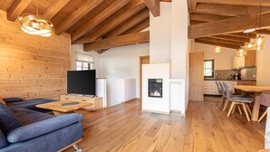 Un salon moderne avec un plafond en bois, une cheminée, un canapé et un coin repas avec des chaises.
